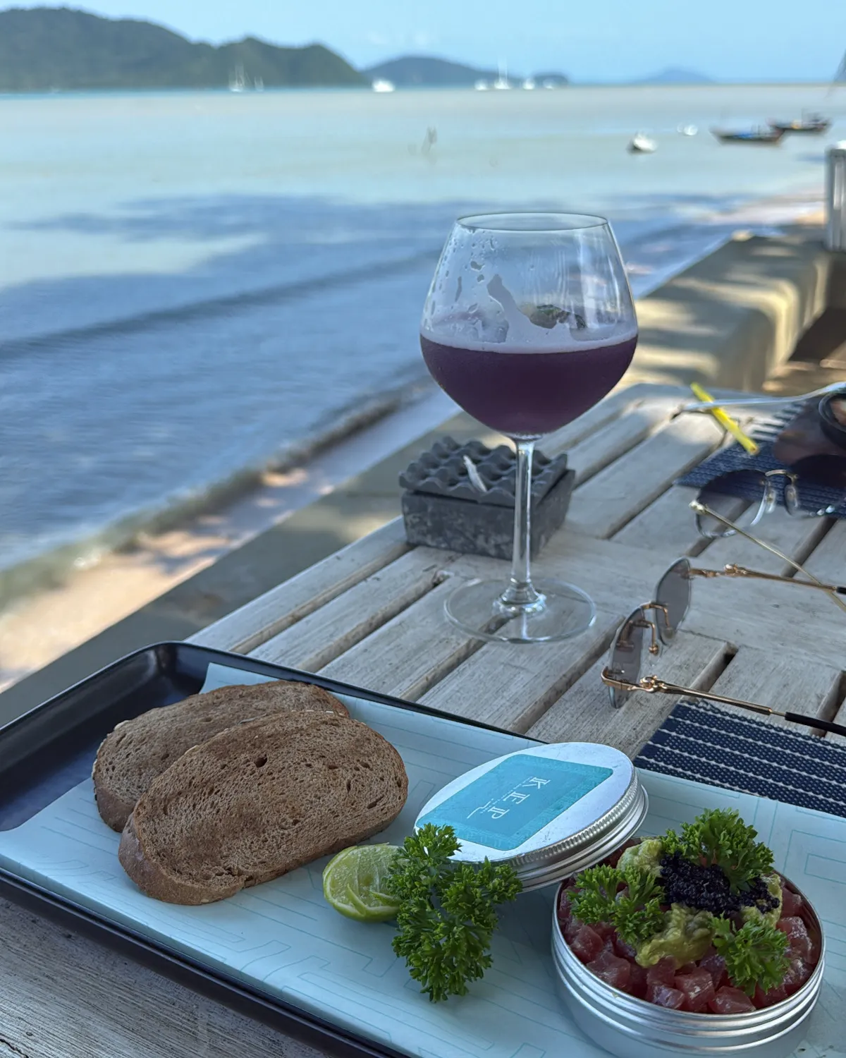 Assiette et verre servis sur une table en bois face à la mer, à Phuket